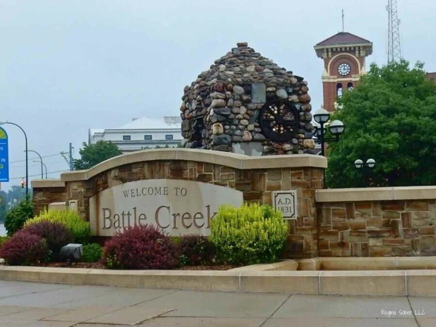 Welcome to Battle Creek sign with stone monument and landscaping, clock tower visible in background