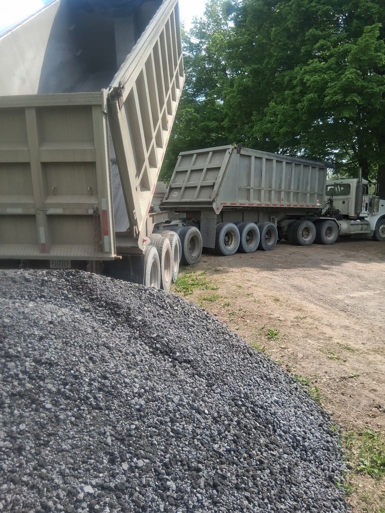 Dump trucks unloading gravel at a construction site with raised beds and green trees in background