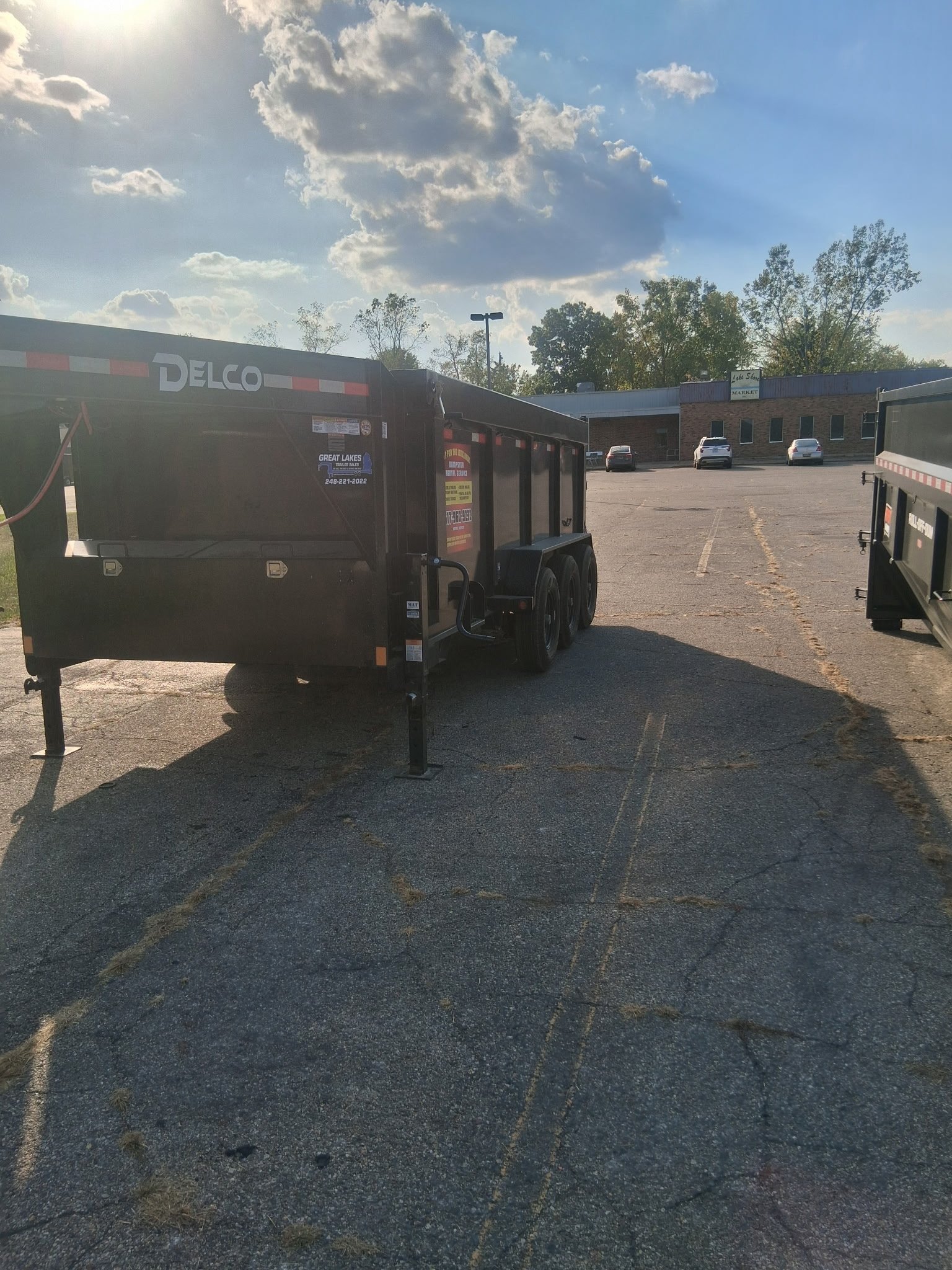 DELCO brand dump trailer parked in an outdoor lot with buildings and sky visible in the background